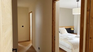 A hallway leading to a bedroom with a bed, bedside lamp, and a hanging light fixture. - Parenthèses A12 by Avecoeur (Huez)