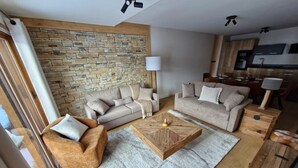 A modern living room with a stone wall, two sofas, a coffee table, and a kitchen in the background. - Parenthèses A12 by Avecoeur (Huez)