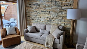 A living room with a stone wall, a grey sofa, a wooden coffee table, and a lamp. - Parenthèses A12 by Avecoeur (Huez)