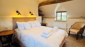Un dormitorio con una cama grande, una silla de madera, una mesita y una ventana con vistas.