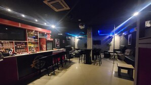 Zona de bar con mostrador, estantes llenos de botellas y asientos.