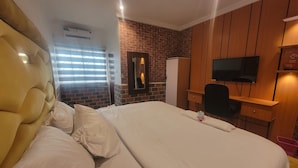 Una habitación de hotel con una cama grande, un armario de madera, un televisor y una pared de ladrillo decorativa.