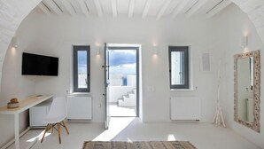 Ένα ευρύχωρο δωμάτιο με λευκό εσωτερικό, ένα μεγάλο παράθυρο, ένα γραφείο, μια καρέκλα και μια τηλεόραση τοποθετημένη στον τοίχο.