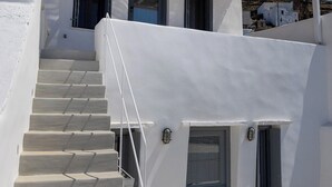 Ένα λευκό κτίριο με μια ξύλινη πέργκολα, μια σκάλα και μια πόρτα.