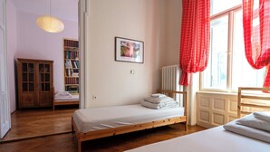 A bedroom with a wooden bed, a wooden wardrobe, a bookshelf, and a window with red curtains. - Trzy Kafki (Kraków)