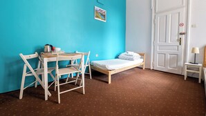 A room with a turquoise wall, a wooden bed, a desk with chairs, and a white door with a no-smoking sign. - Trzy Kafki (Kraków)