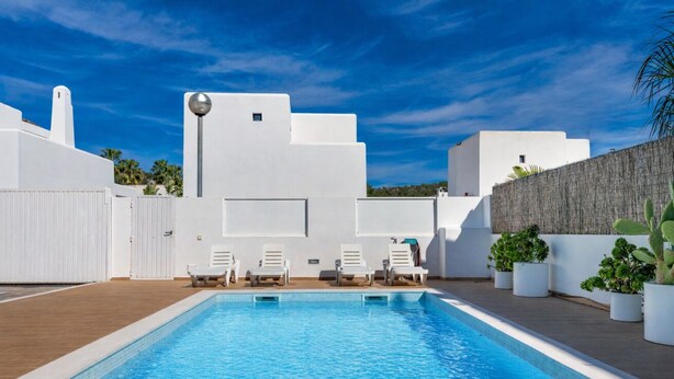 A swimming pool with white lounge chairs, a white building with a flat roof, and a clear blue sky. - New Villa Noa 5 Bedrooms Private Ibiza Escape in Jesús (Santa Eulalia del Riu)