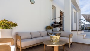 A sunlit outdoor seating area with a sofa, chairs, and a table, accompanied by potted plants and a staircase. - New Villa Noa 5 Bedrooms Private Ibiza Escape in Jesús (Santa Eulalia del Riu)