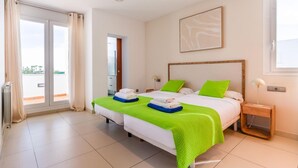 A hotel room with two beds, a sliding glass door to the balcony, a framed abstract painting, and a bedside table with a lamp. - New Villa Noa 5 Bedrooms Private Ibiza Escape in Jesús (Santa Eulalia del Riu)