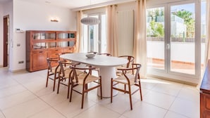 A dining area with a round table and chairs, a wooden cabinet, and a view through a sliding glass door to an outdoor balcony. - New Villa Noa 5 Bedrooms Private Ibiza Escape in Jesús (Santa Eulalia del Riu)