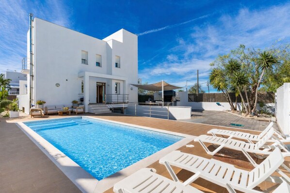 Um edifício moderno branco com piscina e espreguiçadeiras.
