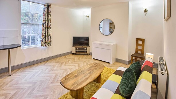 Un salon moderne avec un banc en bois, un canapé coloré, un téléviseur et un radiateur.