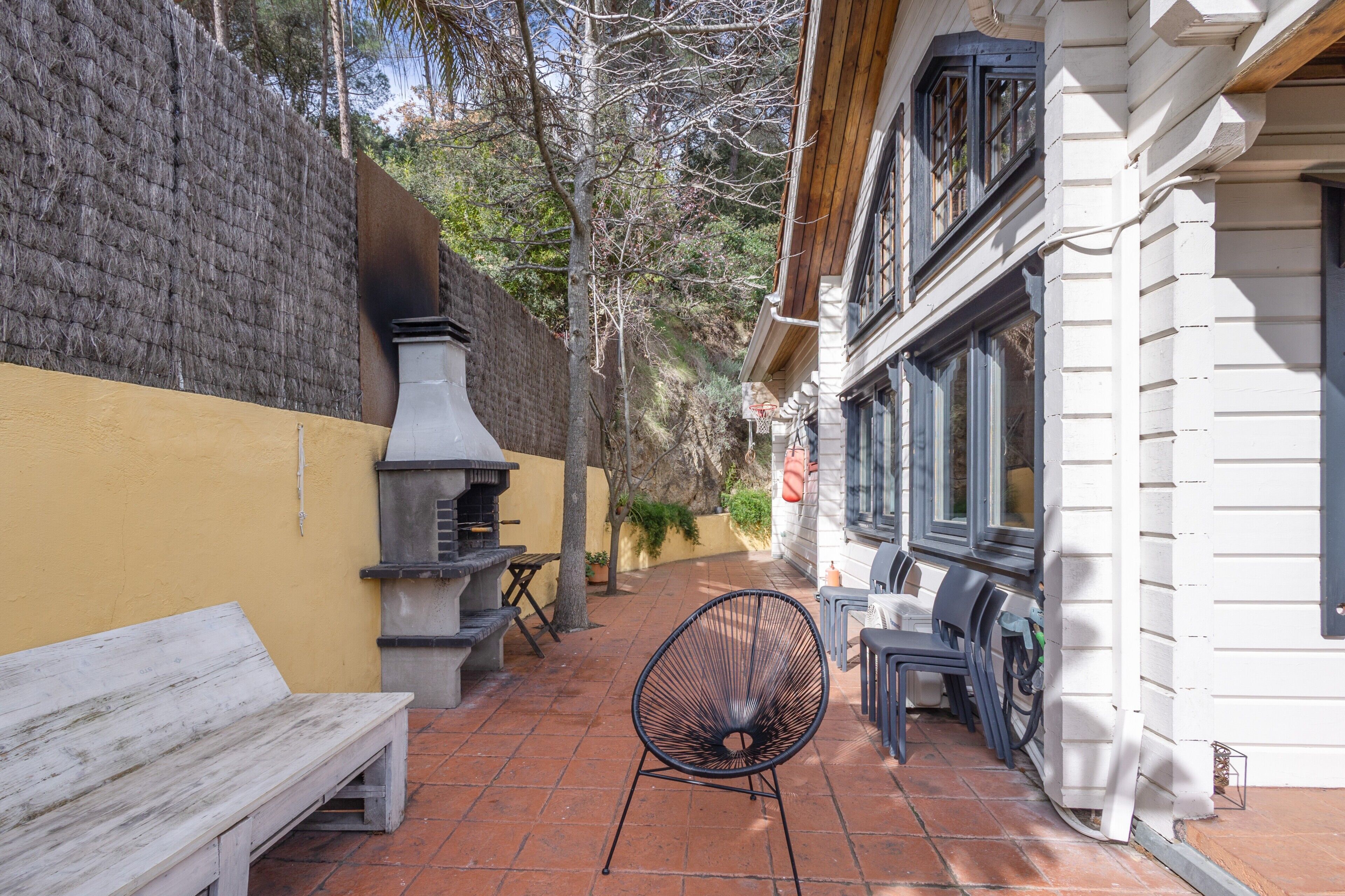 Un patio con un banco de madera, una silla de metal y una parrilla.