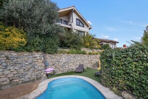 Una casa con piscina, muro in pietra e vegetazione.