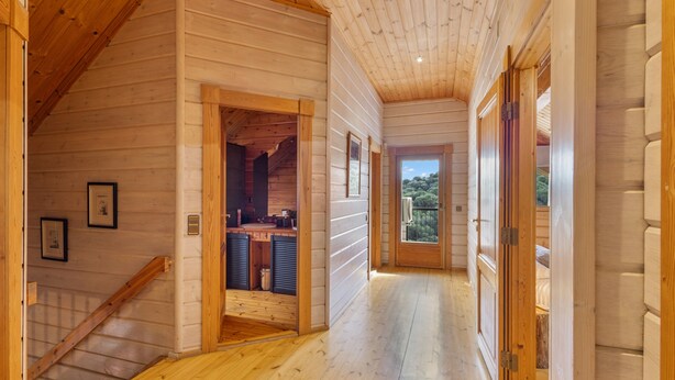 Un intérieur en bois avec un escalier, un coin cuisine et une vue à travers une porte.