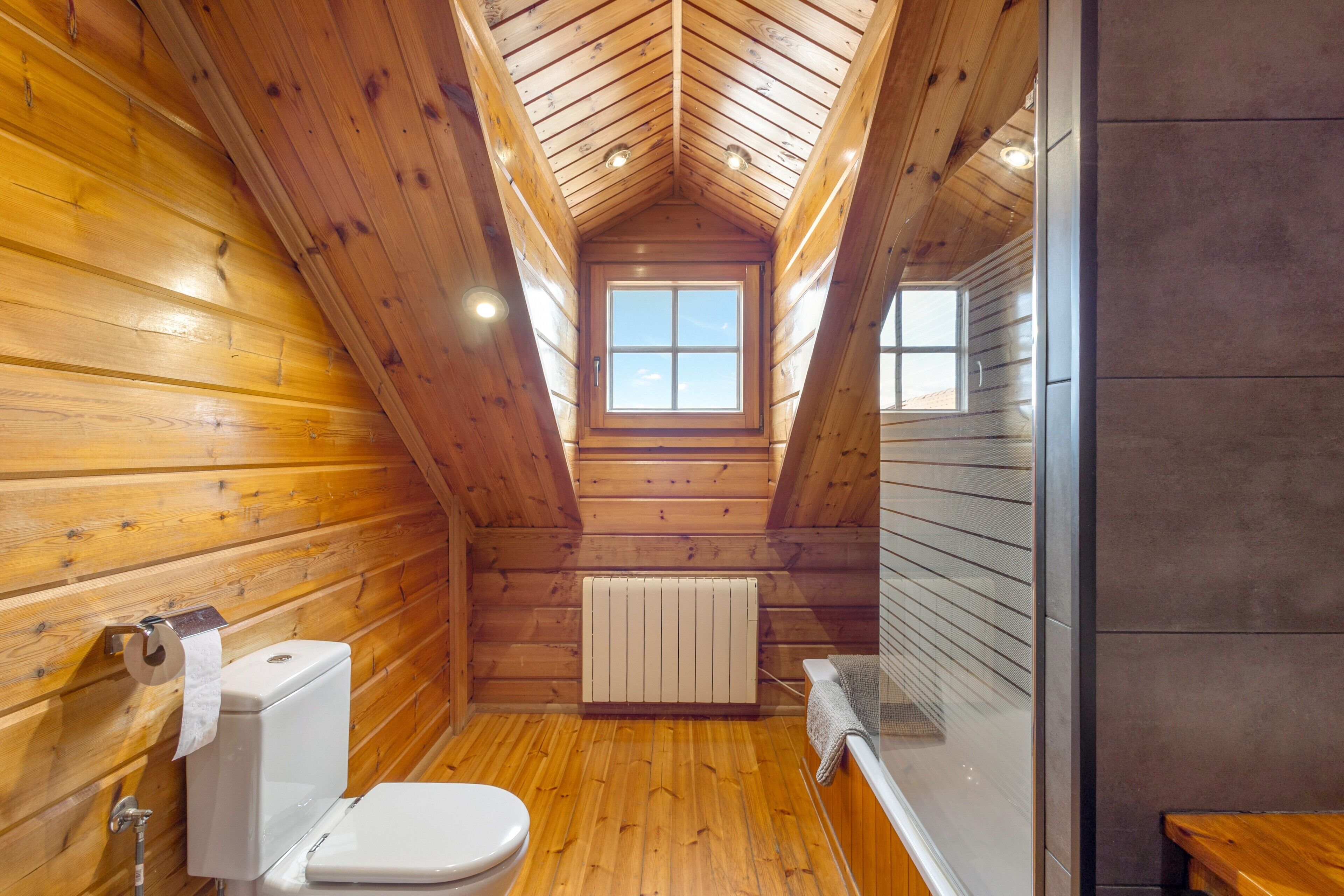 A wooden cabin bathroom with a skylight, toilet, and a radiator.