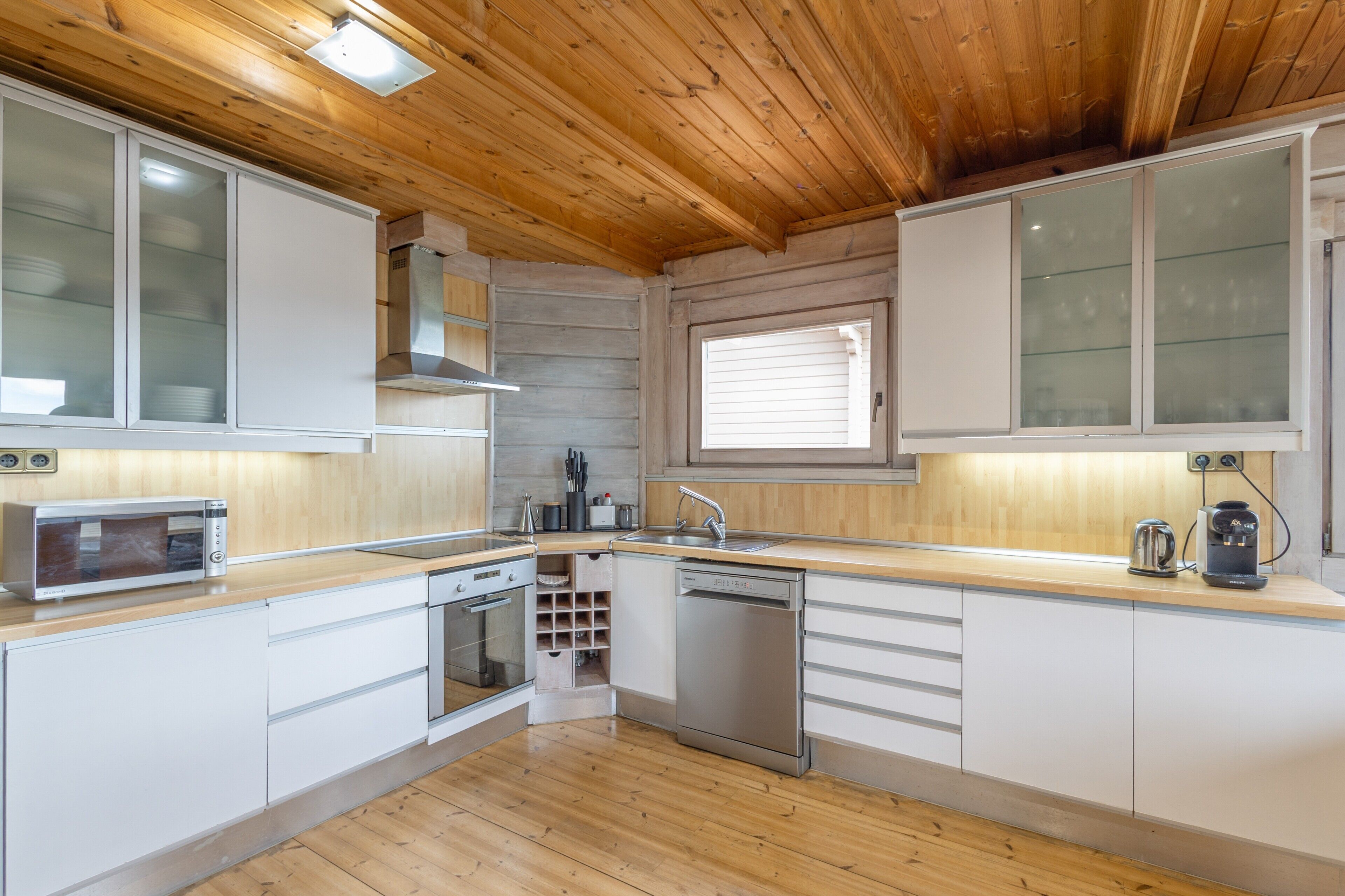 Una cocina moderna con techo de madera, armarios blancos, horno empotrado y lavavajillas.