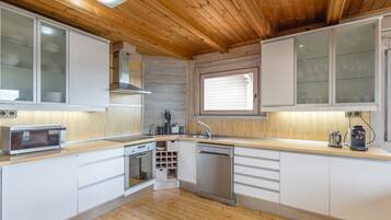 Una cocina moderna con techo de madera, armarios blancos, horno empotrado y lavavajillas.