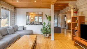 L’intérieur d’un chalet moderne, avec un plafond en bois, un canapé gris, une table basse en bois et une bibliothèque agrémentée d’objets décoratifs.