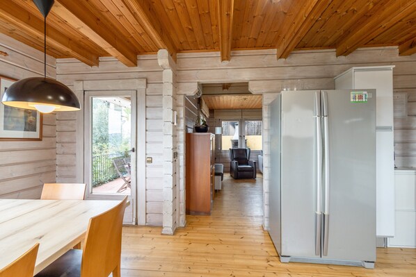Un intérieur en bois comprenant une table à manger, des chaises, un réfrigérateur et une vue sur l’extérieur.