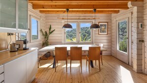 Une cabane en bois avec une table à manger, des chaises et une vue sur la forêt, visible à travers de grandes fenêtres.