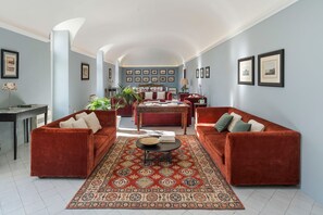 Un salon spacieux avec un canapé en velours rouge, un tapis à motifs et un coin repas comprenant une table et des chaises.
