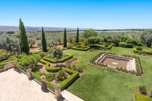 Un jardin aménagé avec des haies aux formes géométriques, une place centrale et une vue sur des collines lointaines.