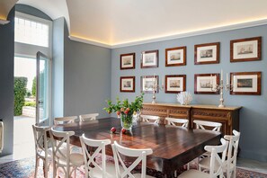 A dining room with a large wooden table, white chairs, a vase with flowers, and framed pictures on the wall.