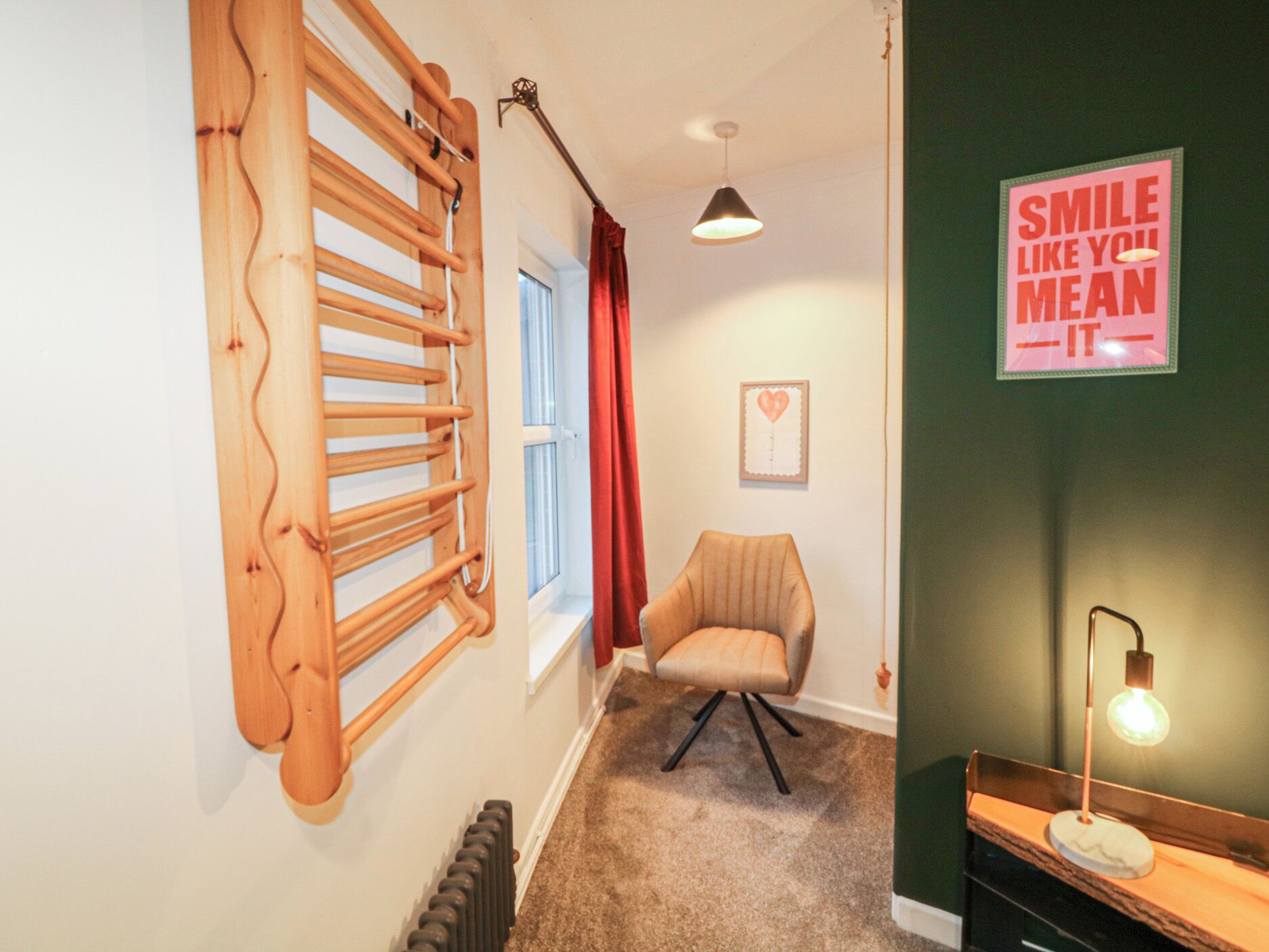 A hallway with a wooden radiator, a chair, a radiator, a wall with a sign, and a ceiling light.