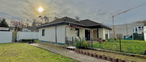 Einbungalow mit Ziegeldach, einer Veranda und einem kleinen Garten.