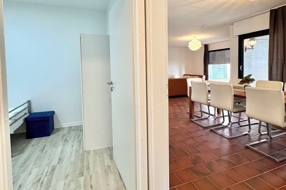 A room with a dining area, a door leading to another room, and a small blue stool.