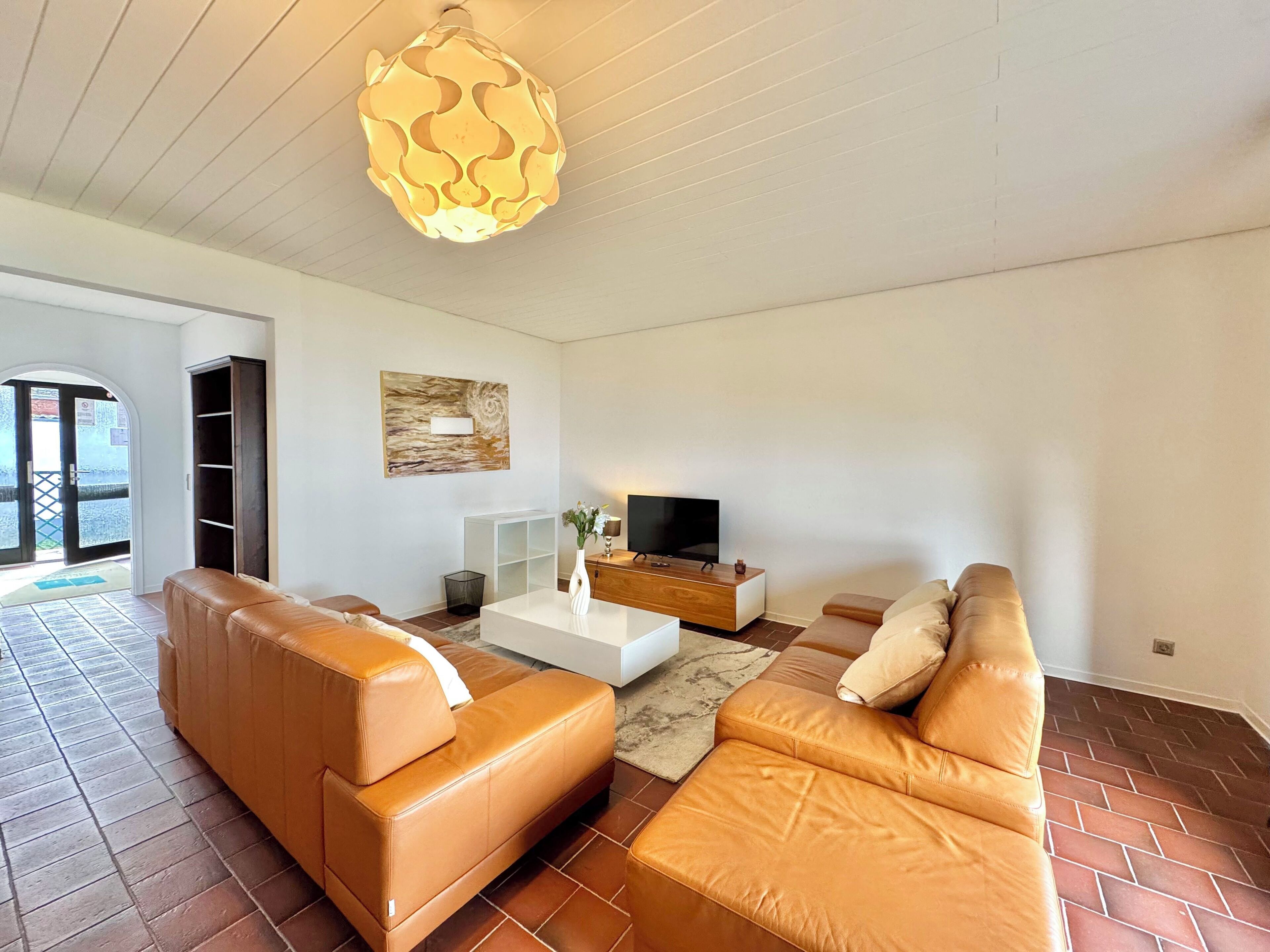 A modern living room with leather sofas, a flat-screen TV, and a unique ceiling light fixture.