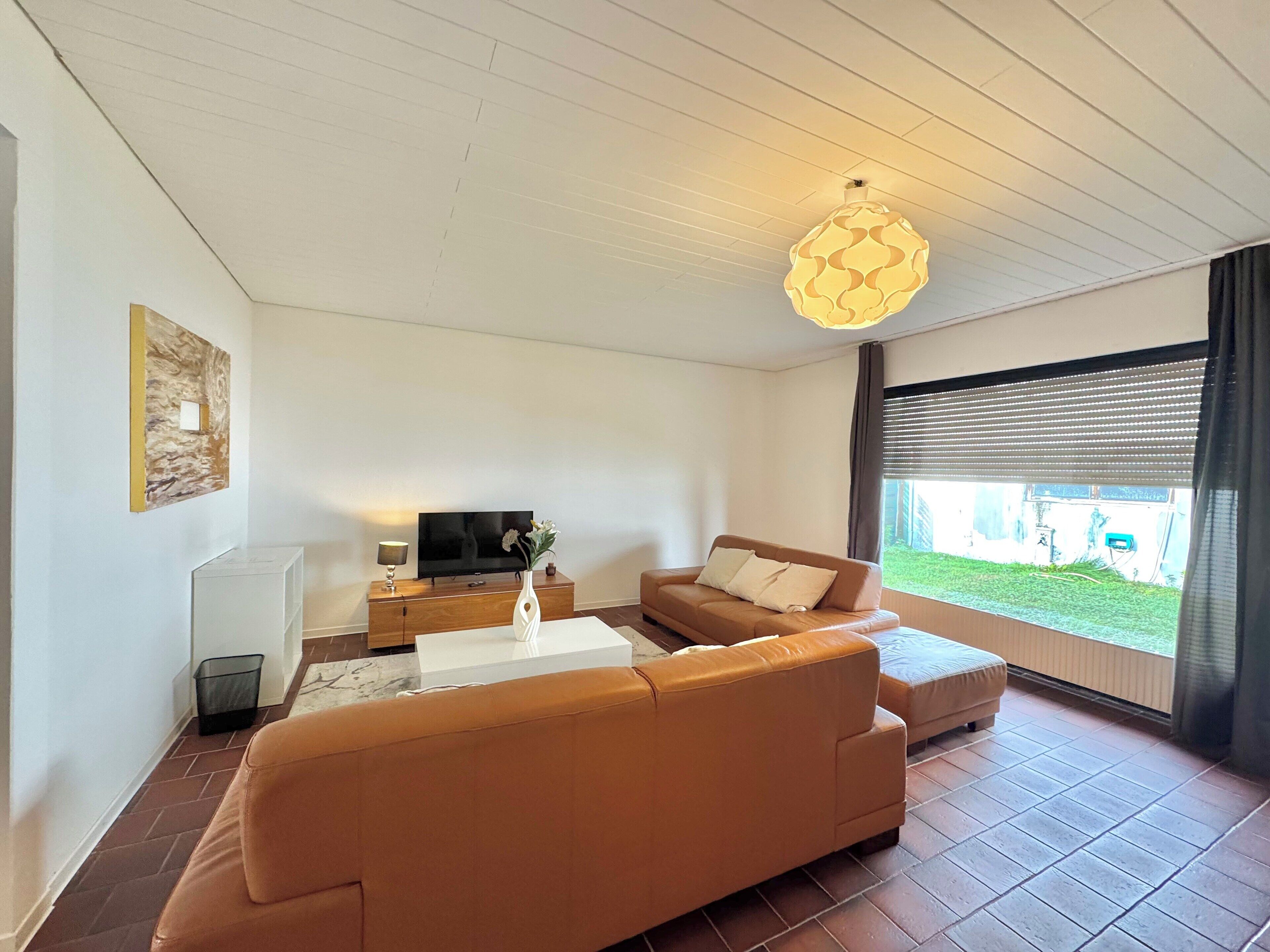 Een moderne woonkamer met een bank, salontafel, televisie en een decoratieve vaas.
