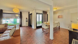 Ein geräumiger Wohnbereich mit einer Sofagarnitur, einem Esstisch mit Stühlen und einer Glasschiebetür, die auf einen Balkon führt.