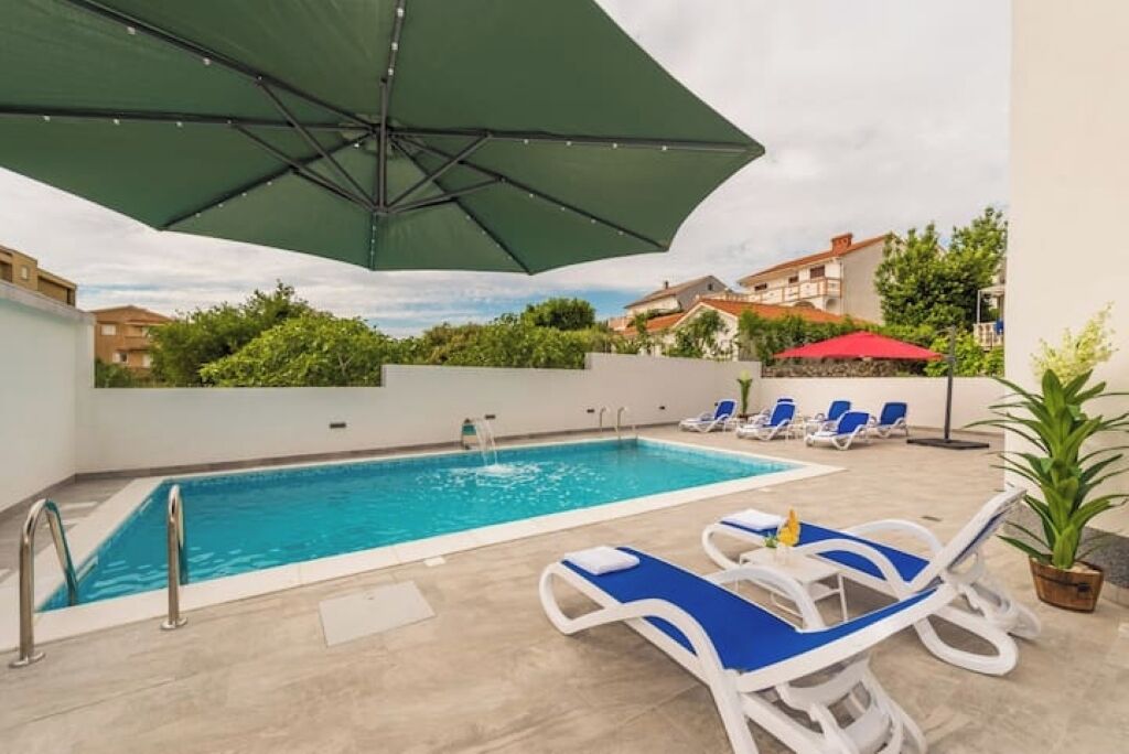 Piscina com espreguiçadeiras, um guarda-sol verde e uma cascata.