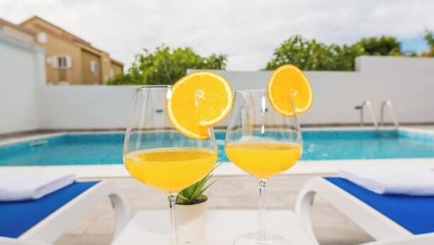 Two glasses of orange juice on a poolside lounge chair with a pool in the background. - Villa Jana 1 (Novalja)