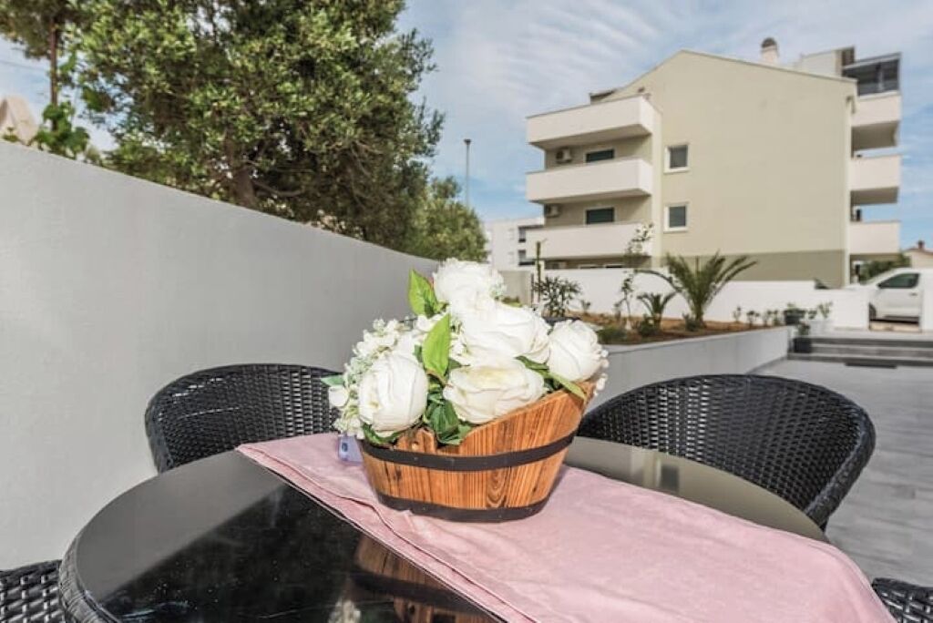 Een tafel met een rieten mand vol witte bloemen, zwarte rieten stoelen en een roze tafelkleed.