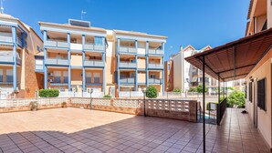 Un immeuble résidentiel à plusieurs étages, doté de balcons, d’un patio couvert et d’une cour dallée.