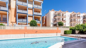 Une piscine décorée avec des motifs de dauphins, entourée d’immeubles à plusieurs étages dotés de balcons.