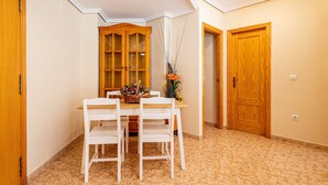 Un coin repas comprenant une table en bois, des chaises blanches, un buffet et un vase avec des fleurs.