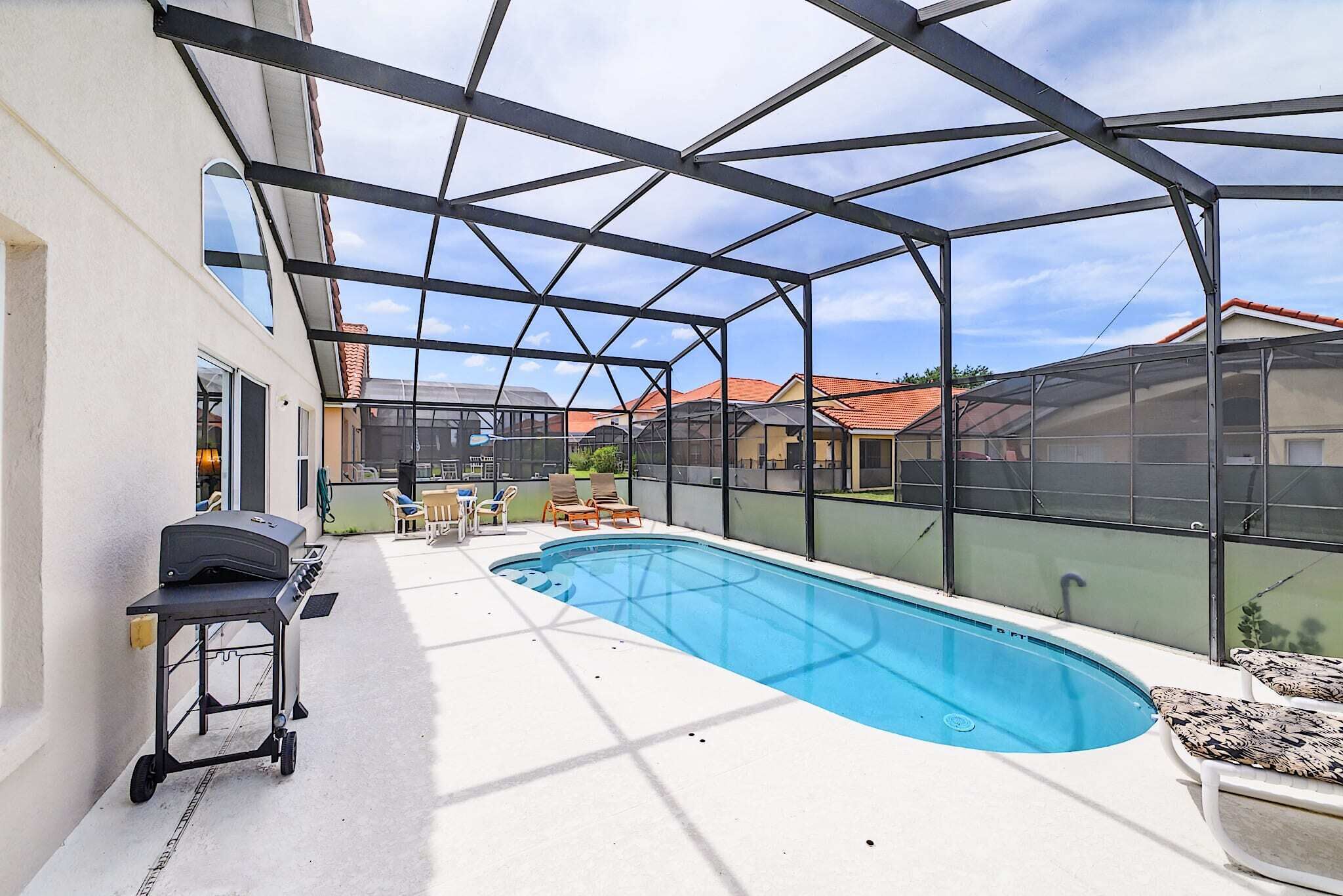 A covered outdoor swimming pool with a grill and lounge chairs.