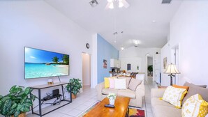 A living room with a TV, sofa, coffee table, and plants. - Family Resort Home w Pool BBQ Game Room (Davenport)