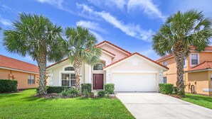 A two-story house with a garage, surrounded by well-maintained lawns and palm trees. - Family Resort Home w Pool BBQ Game Room (Davenport)
