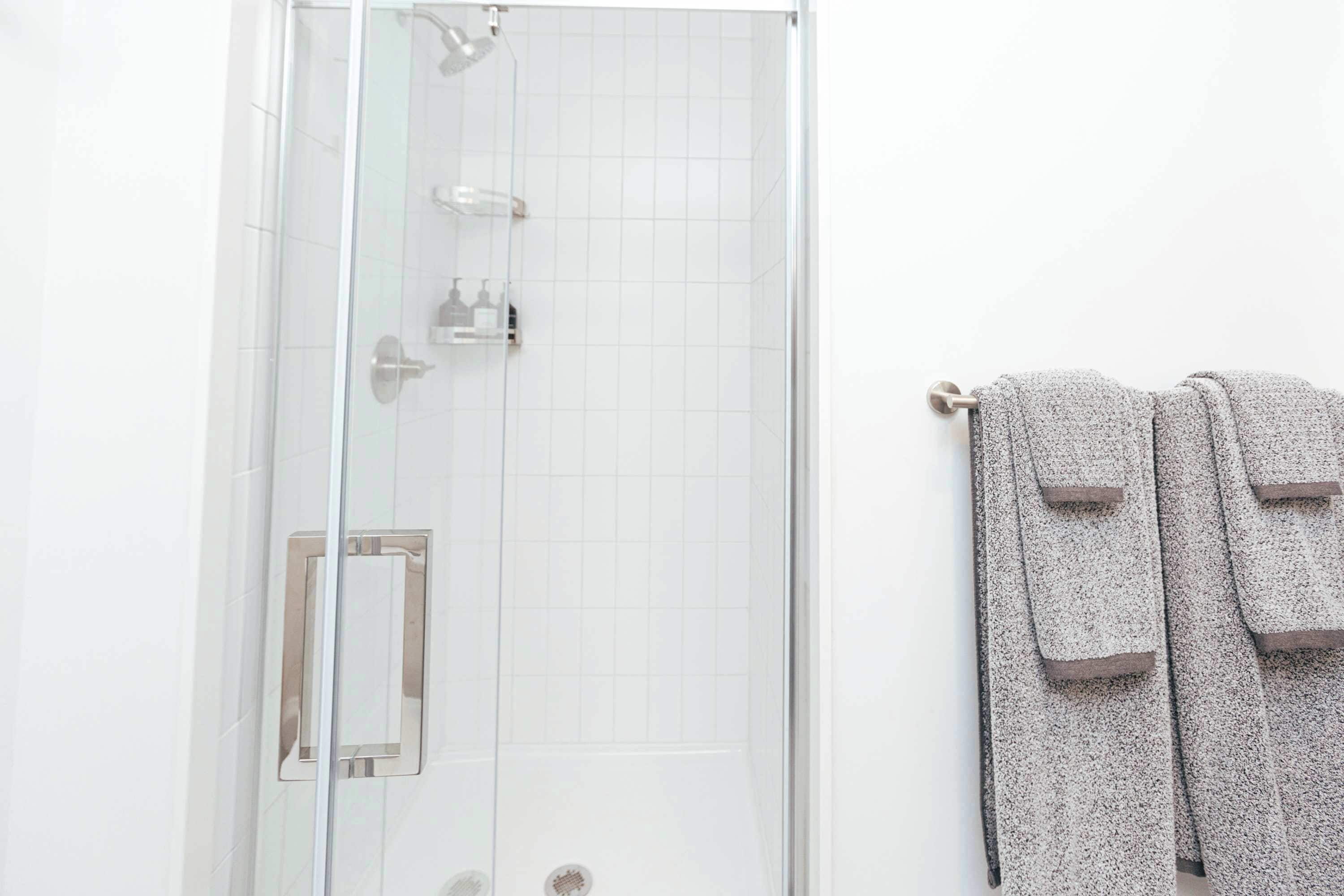A glass-enclosed shower with a white tiled wall, a towel rack with two towels, and a small mirror.