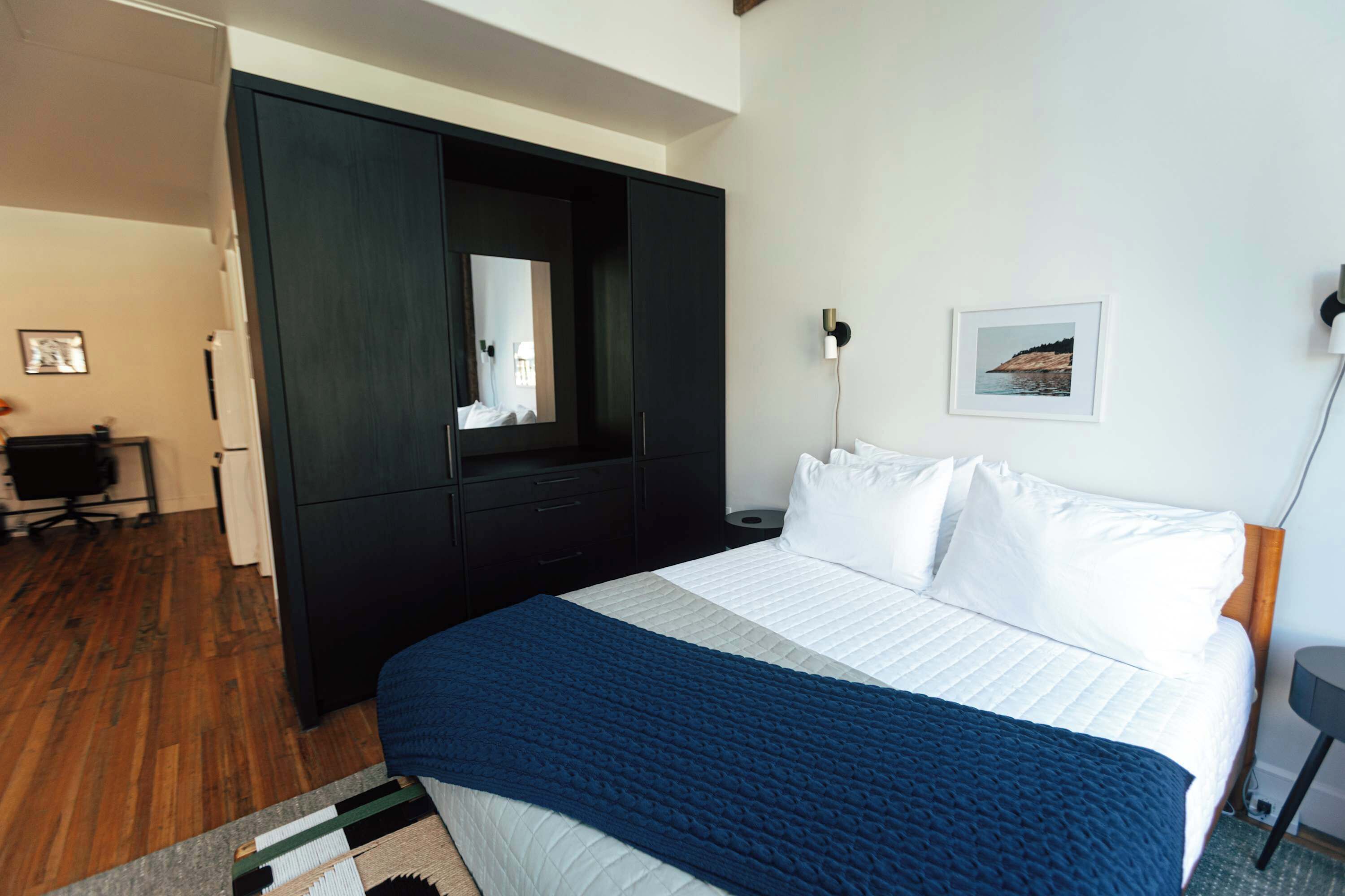 Un dormitorio con una cama grande, un armario oscuro, un espejo, un escritorio y un cuadro en la pared.