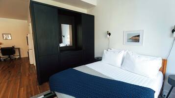 Un dormitorio con una cama grande, un armario oscuro, un espejo, un escritorio y un cuadro en la pared.
