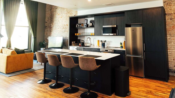 Una cucina moderna con isola centrale, sgabelli da bar, frigorifero e parete decorata con mattoni.