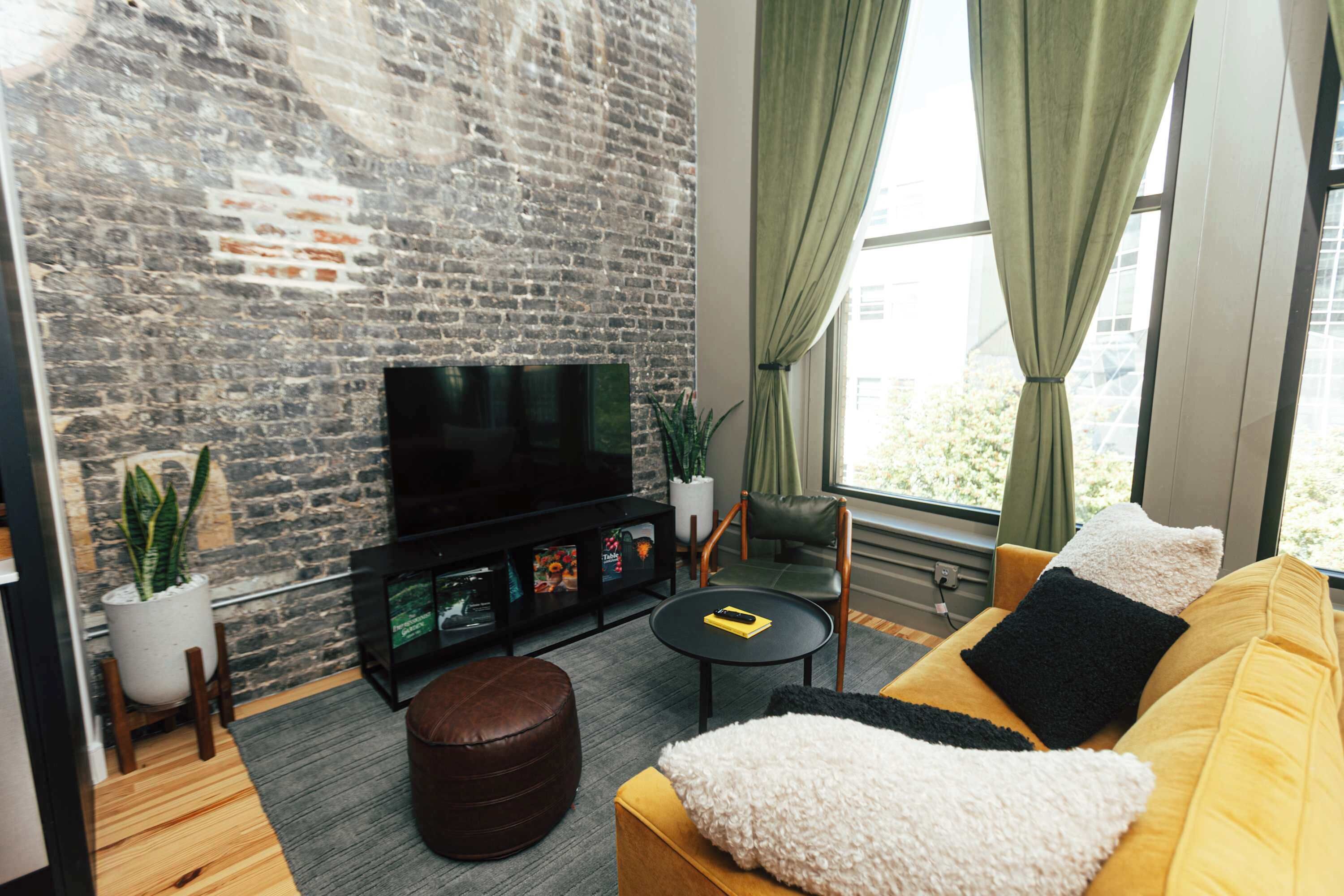 A modern living room with a brick wall, a flat-screen TV, a yellow sofa, and a small round table.