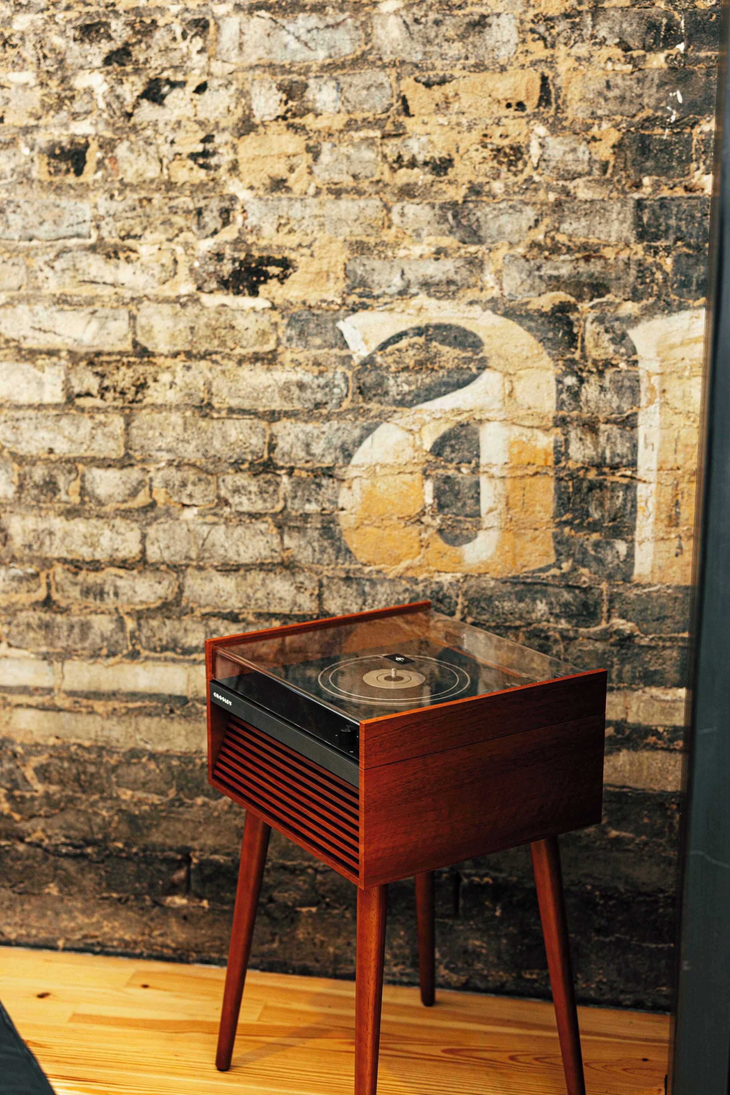 Tocadiscos antiguo sobre un soporte de madera frente a una pared de ladrillo con textura.