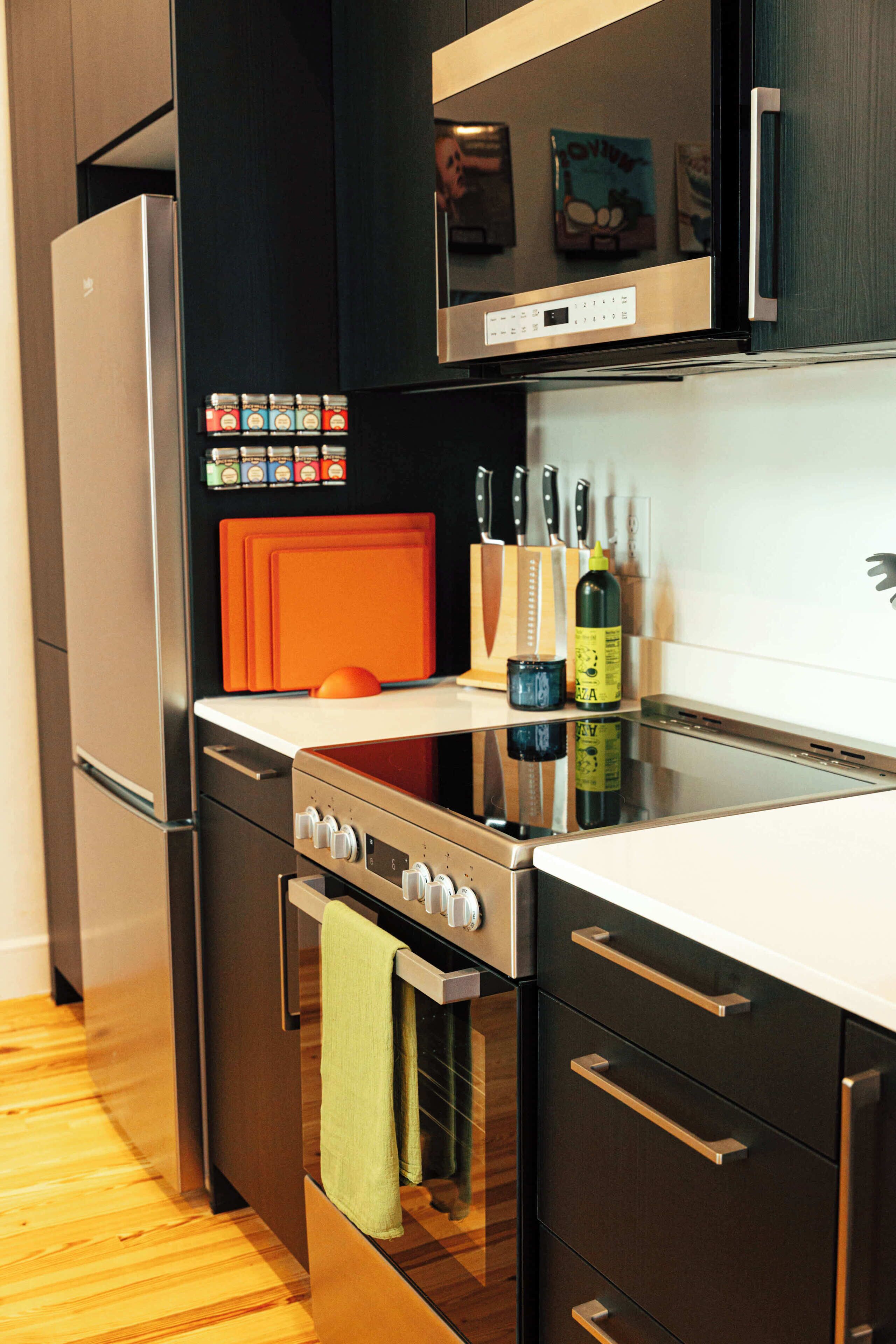 A modern kitchen with stainless steel appliances, wooden flooring, and a black cabinet with a microwave above the stove.